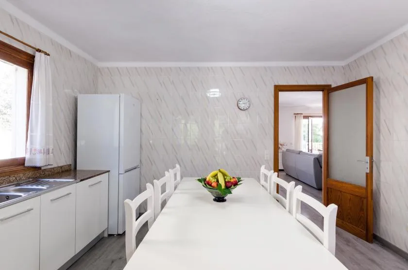 A dining room with a long white table and a kitchen along one wall.