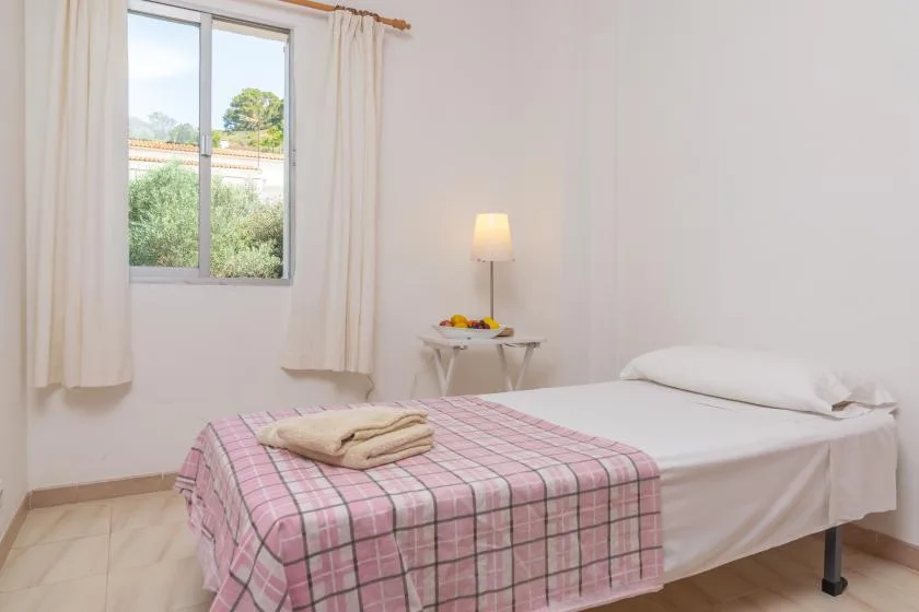 A bedroom with a single bed, a bedside table, and a curtained window.