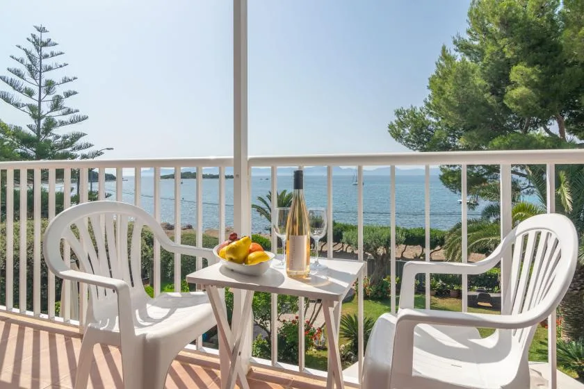 A balcony with white seating and a small table overlooks the sea.