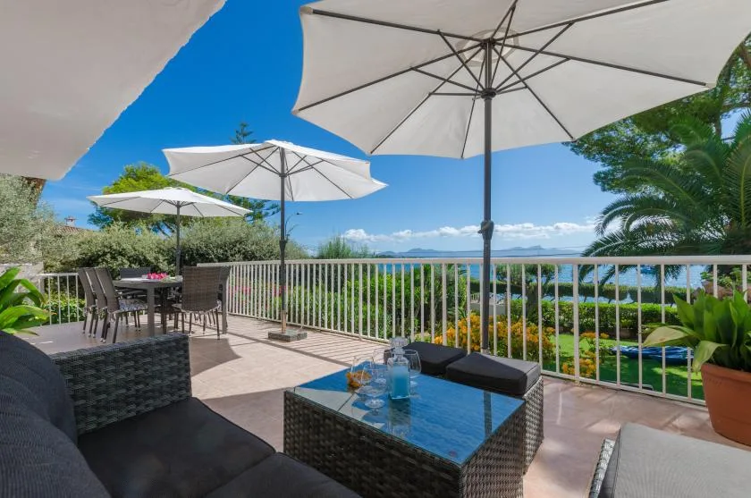 An outdoor terrace has seating beneath umbrellas and a view over greenery.