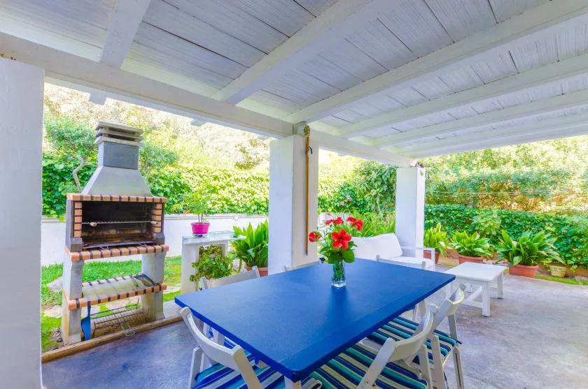 A covered outdoor dining area with a blue table and a brick barbecue.