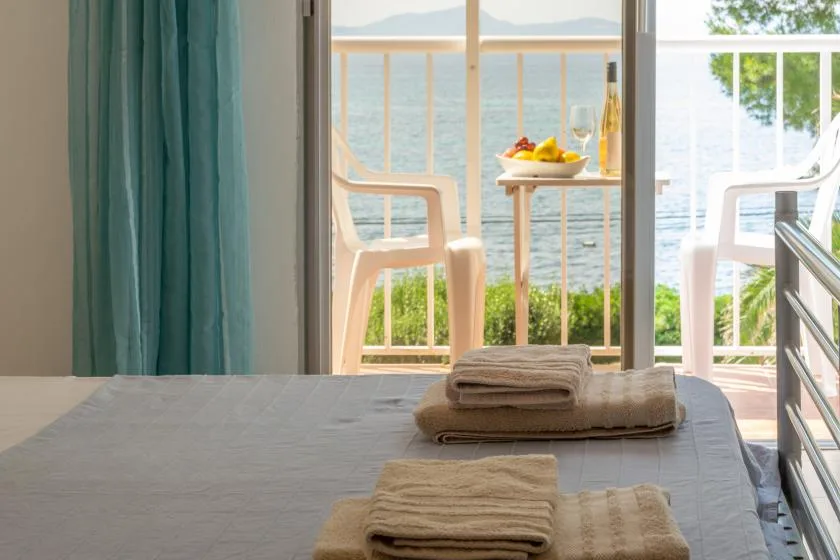 A bedroom opens onto a balcony with seating and a view of the water.