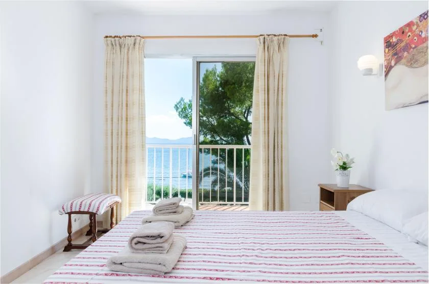 A bright bedroom with a striped bed and a balcony view of the water.
