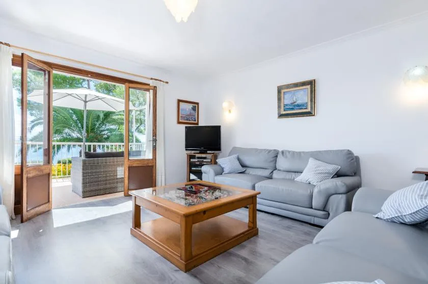 A living room with gray seating and a wooden coffee table beside open glass doors.