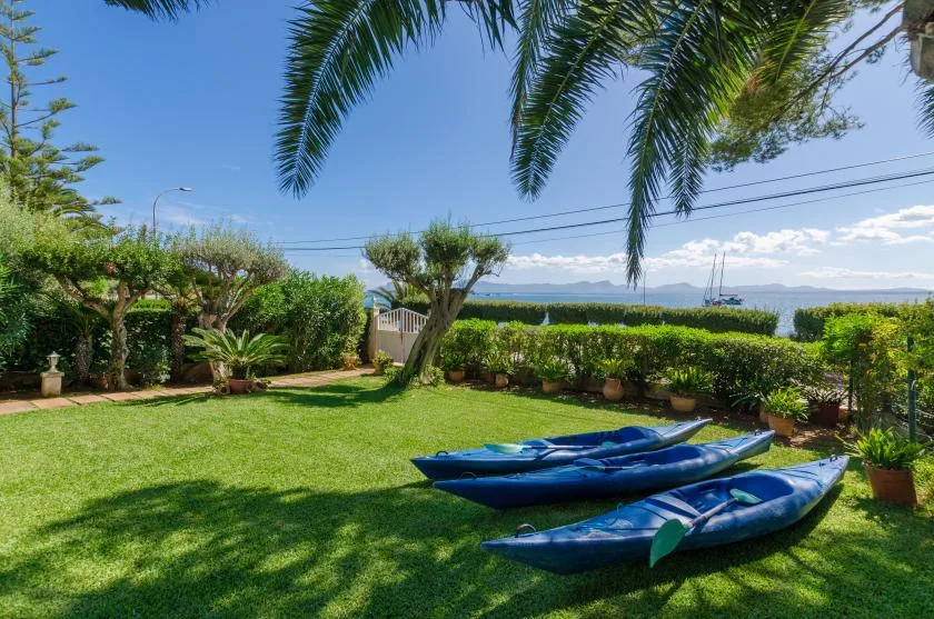 A grassy garden with blue kayaks, leafy trees, and a view of the sea.