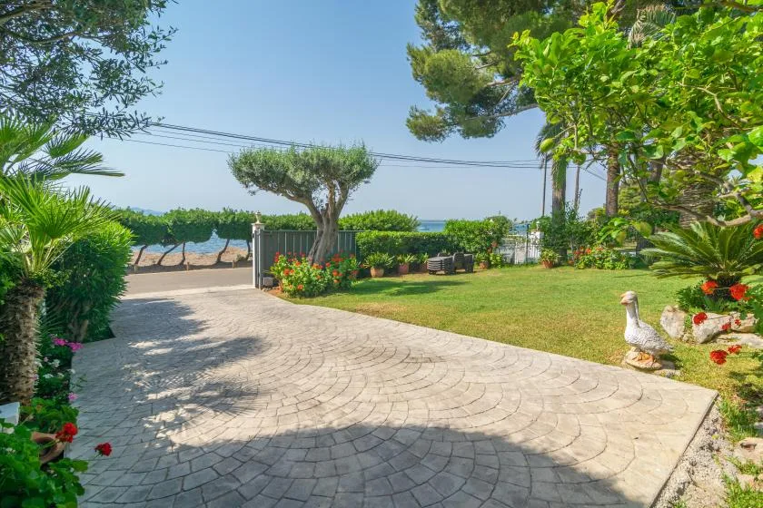 A paved garden path curves past trimmed greenery toward a view of the sea.