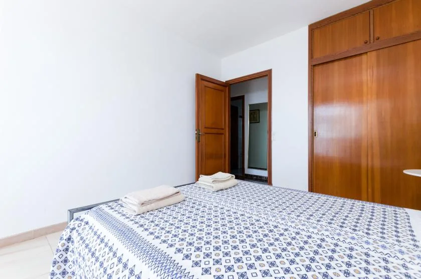 A bedroom with a bed covered in patterned bedding and a wooden wardrobe.