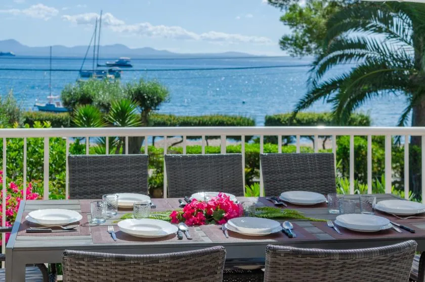 A dining table on a terrace overlooks the sea and distant mountains.