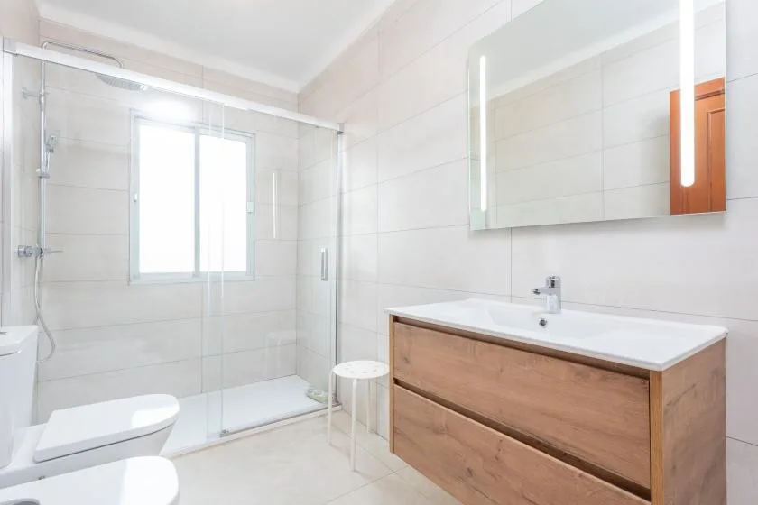 A bright bathroom with a glass shower, sink, and wood-toned vanity.