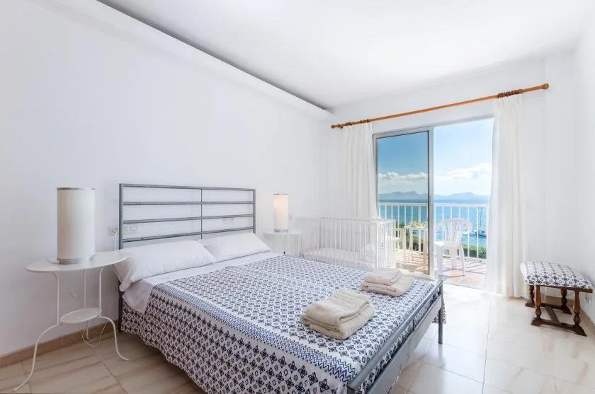 A bright bedroom with a patterned bed and sliding glass doors opening to a balcony.