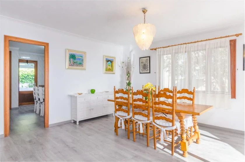 A bright dining room with a wooden table and chairs beside a large curtained window.