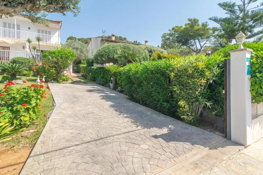 A paved driveway runs between landscaped gardens and a white building.