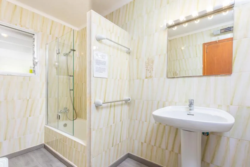 A bright bathroom with a glass shower, wall mirror, and pedestal sink.