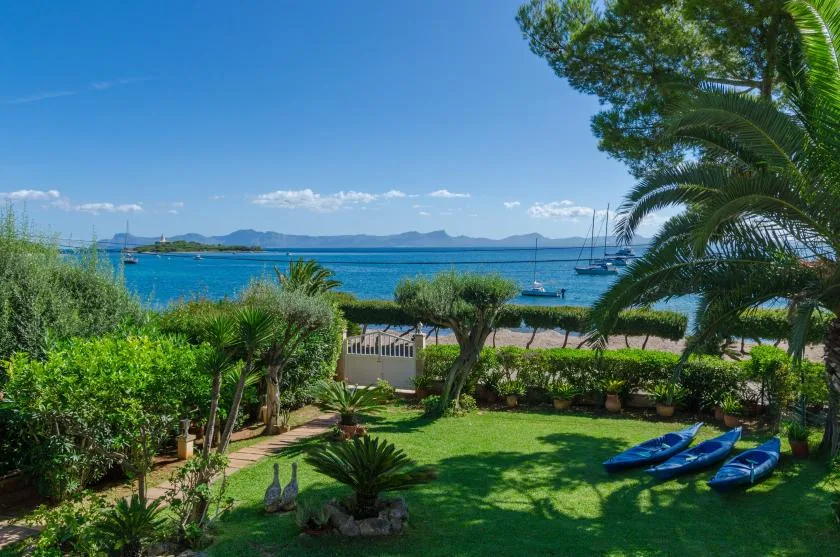 A landscaped garden overlooks a blue bay with boats and distant hills.