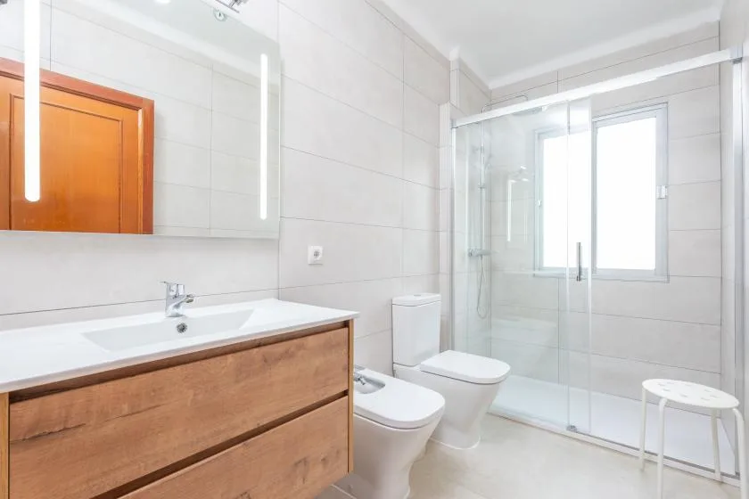A bright tiled bathroom with a wooden vanity and glass shower.
