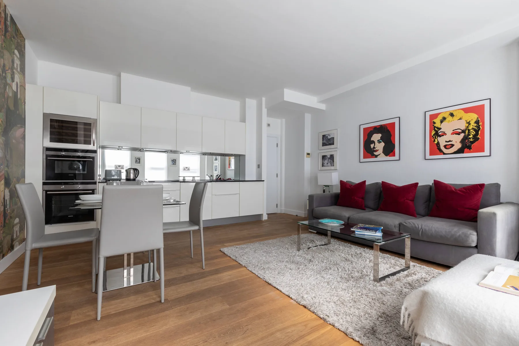 A bright open-plan living room and kitchen with red cushions on the sofa.