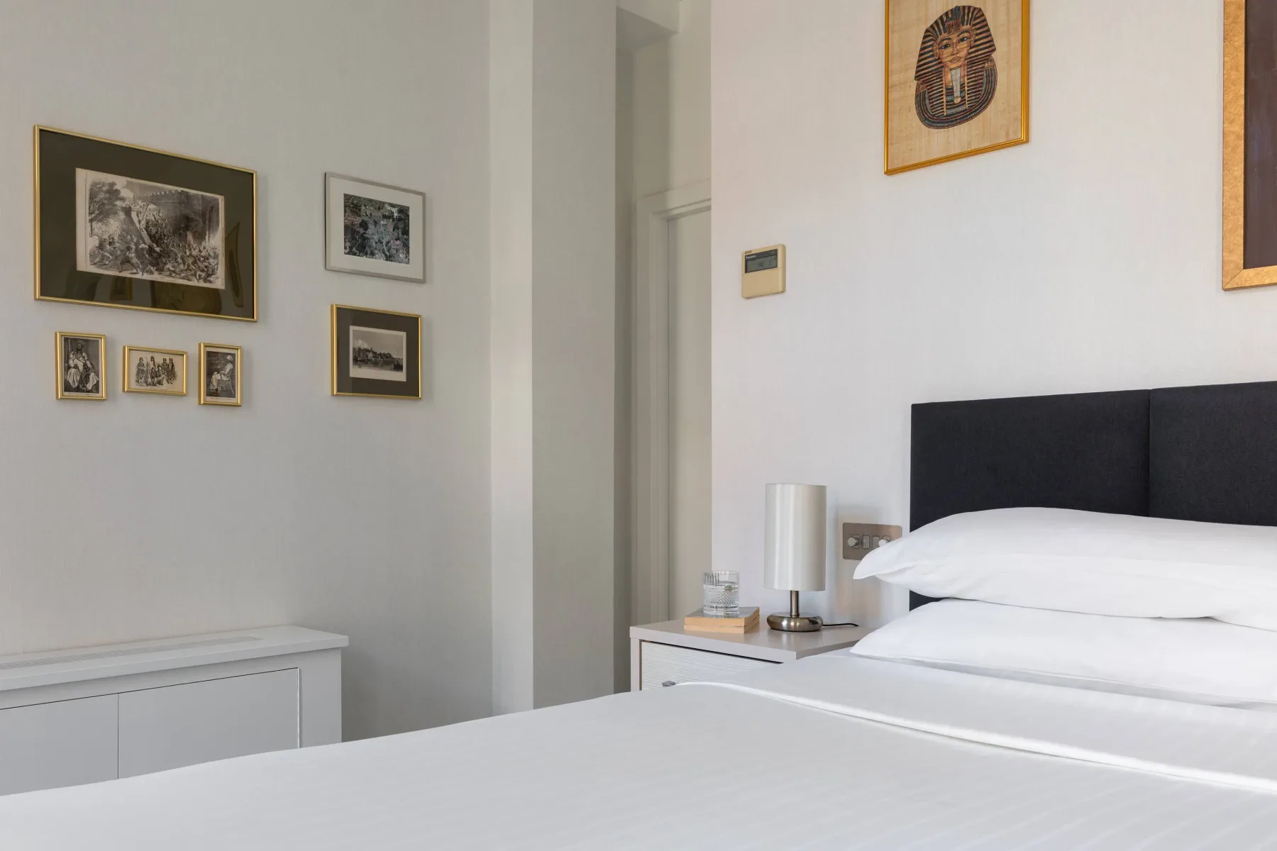 A bright bedroom with a bed, bedside table, and framed artwork on the walls.