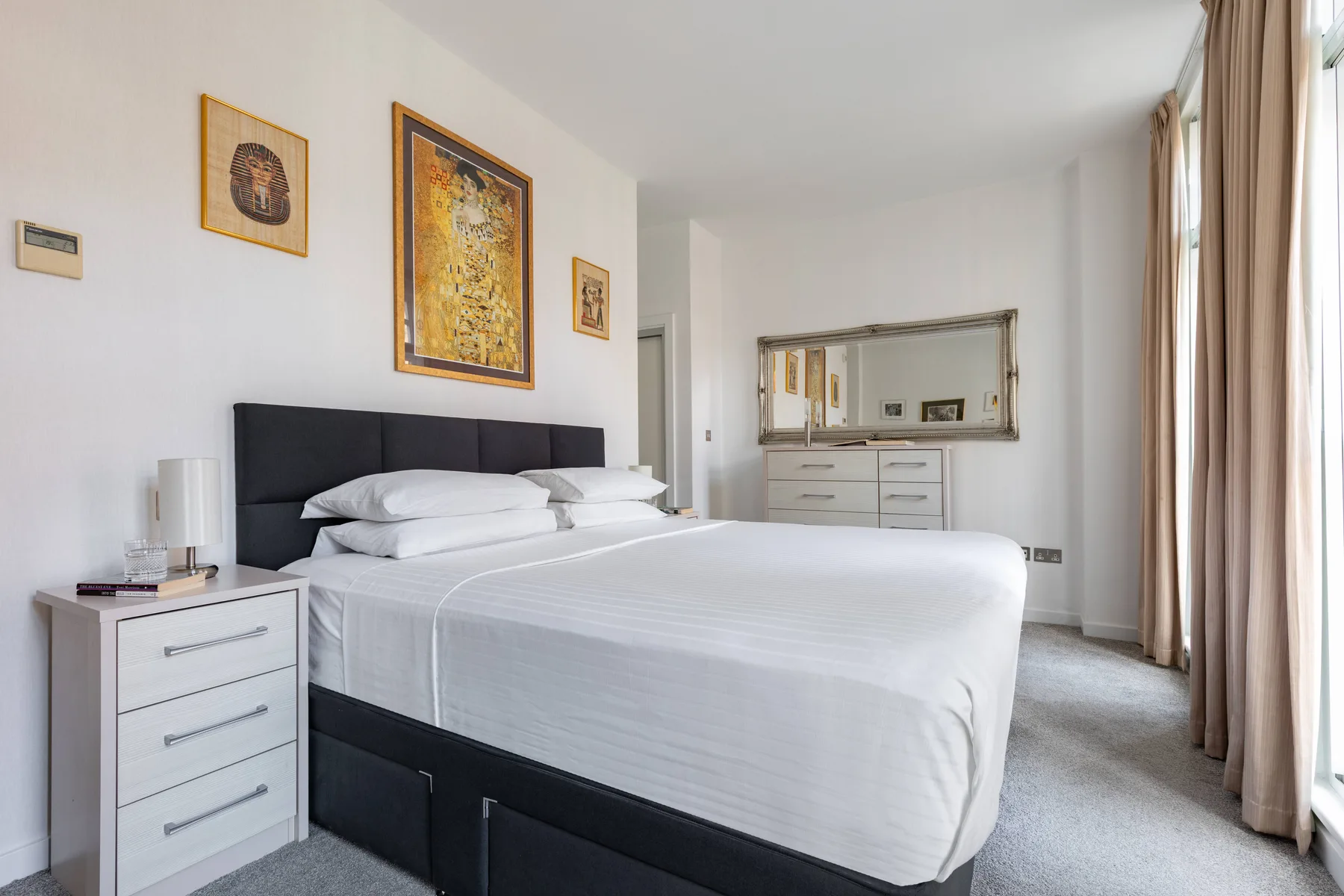 A bedroom with a neatly made bed and a dresser beneath a wall mirror.