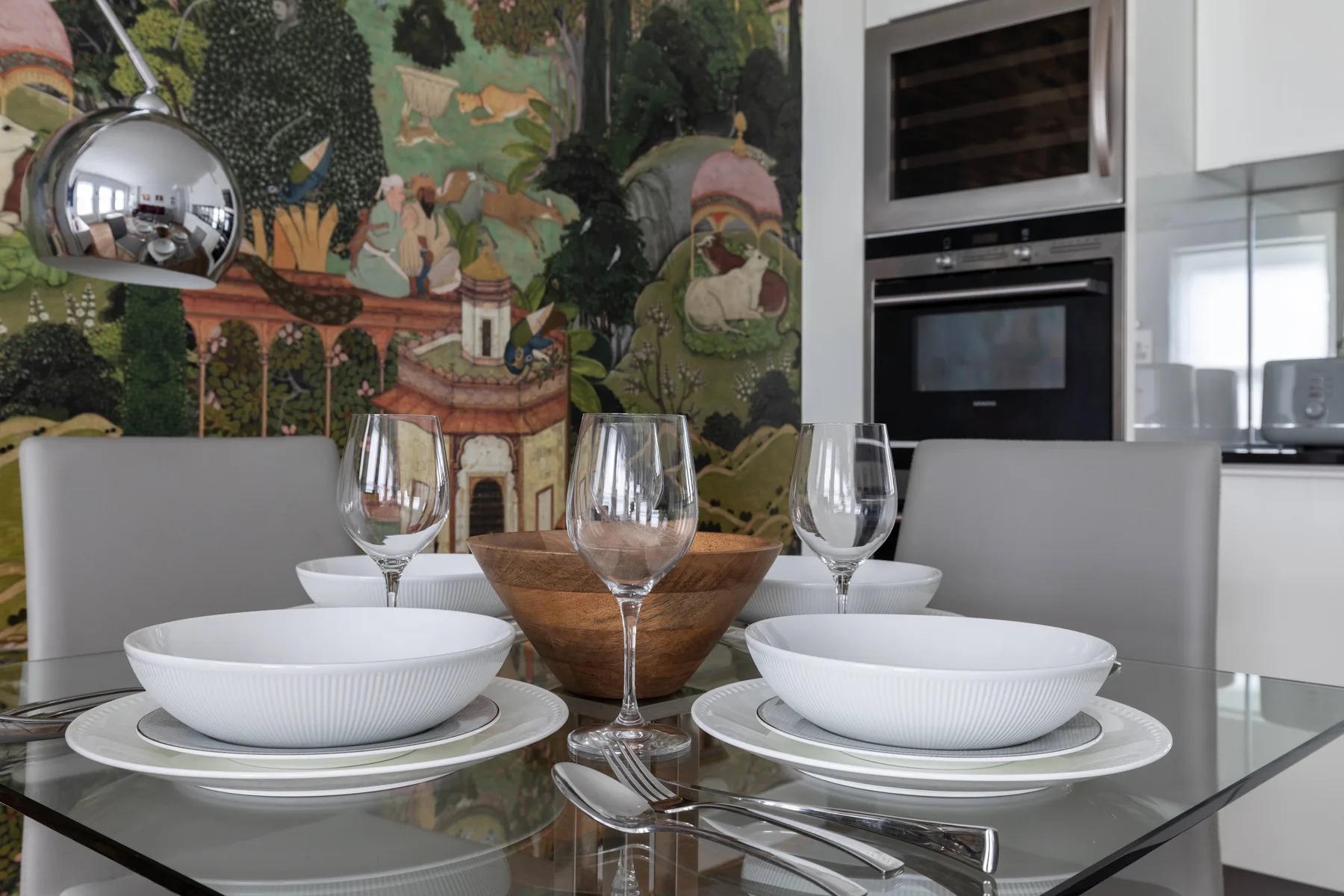 A dining table is set with plates and glasses in a modern kitchen.