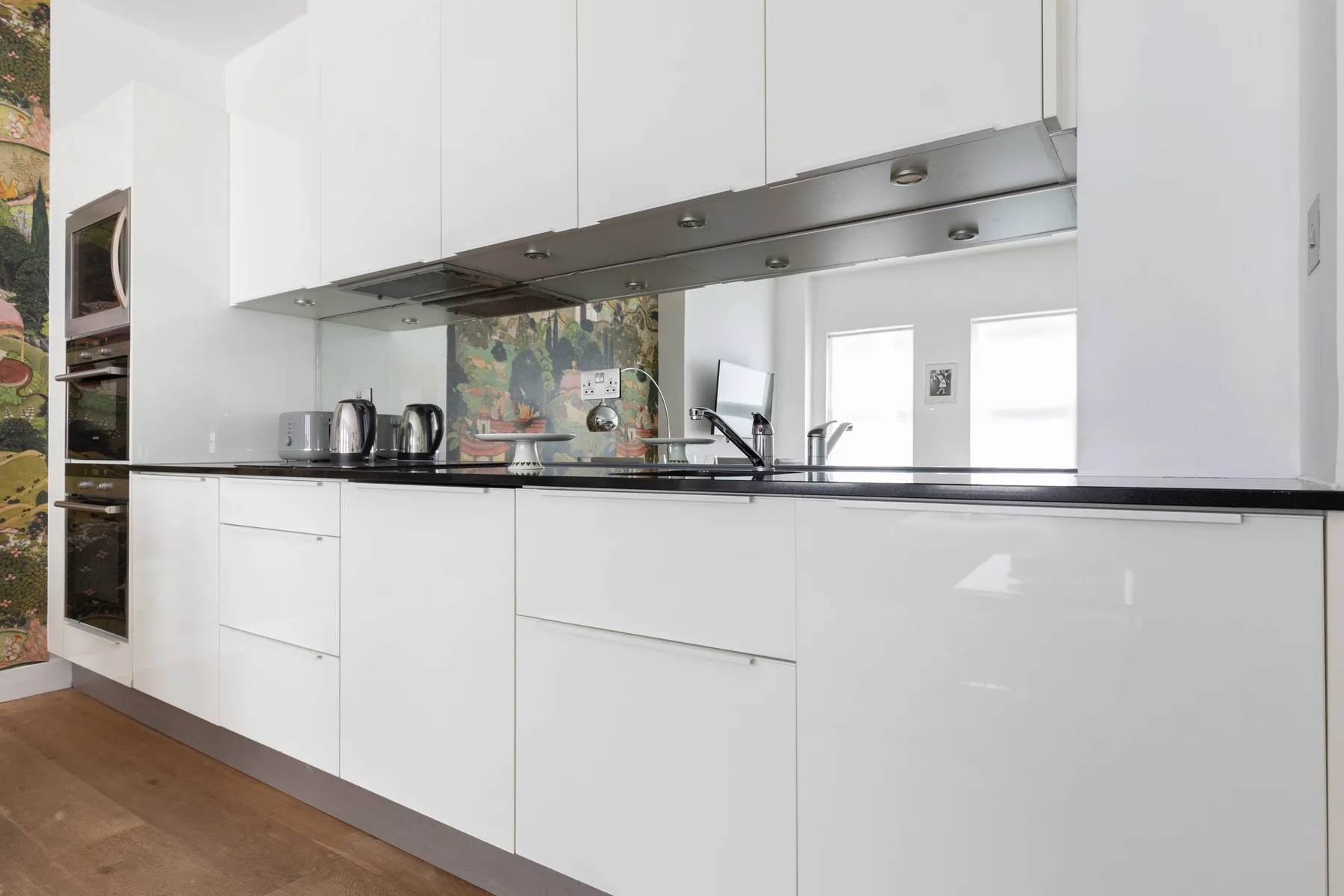 A modern white kitchen with a long counter, sink, and built-in appliances.