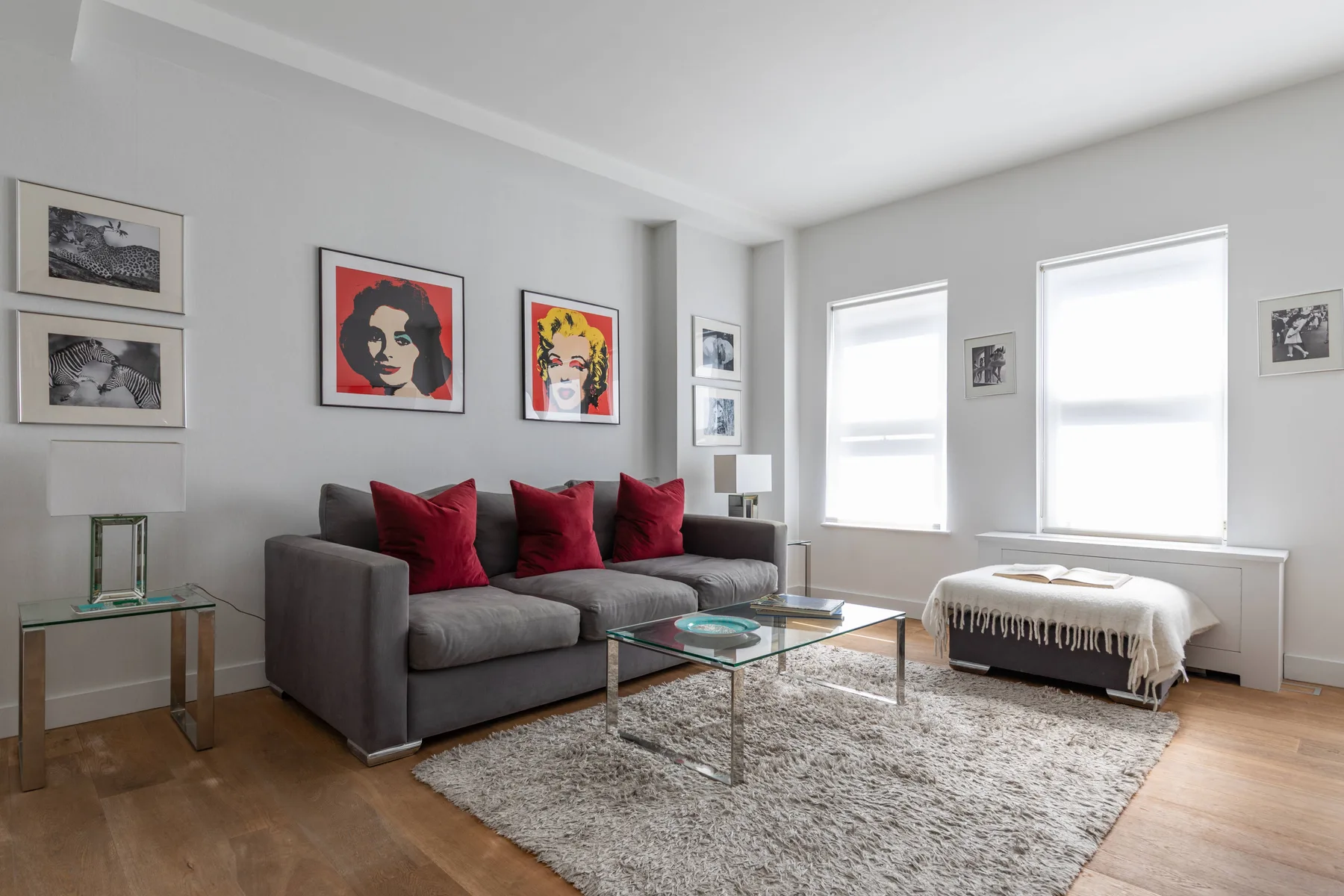 A bright living room with gray seating, a glass coffee table, and large windows.