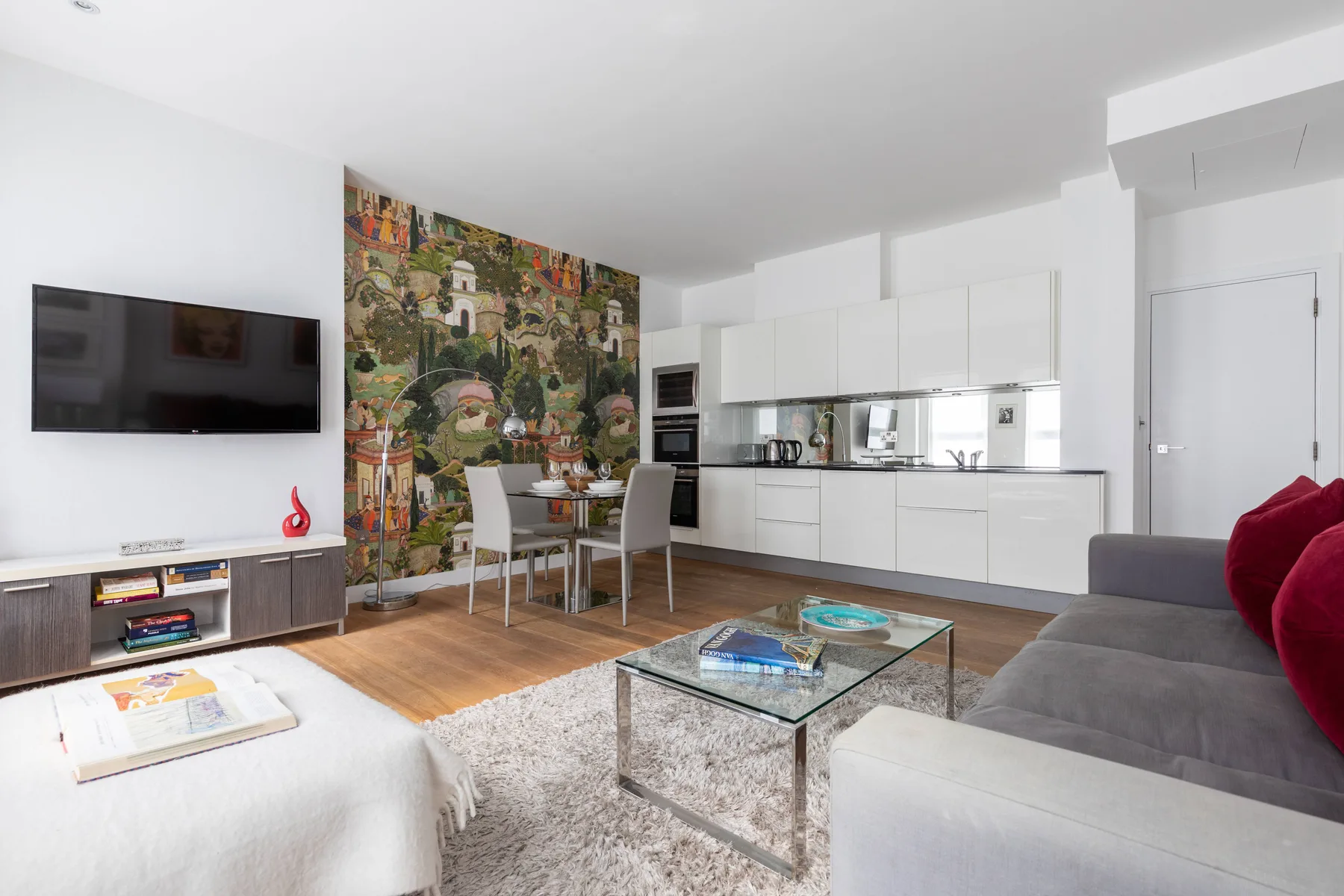 A bright open-plan living room and kitchen with a dining table and gray seating.