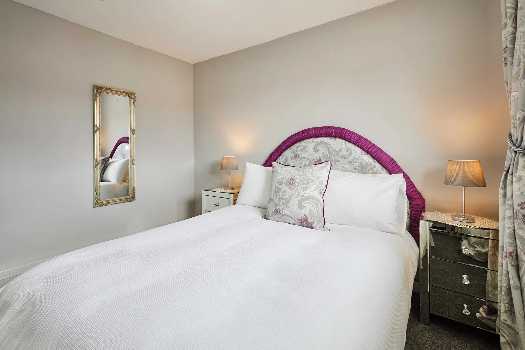 Un dormitorio con una cama blanca, cojines estampados y lámparas junto a la cama.