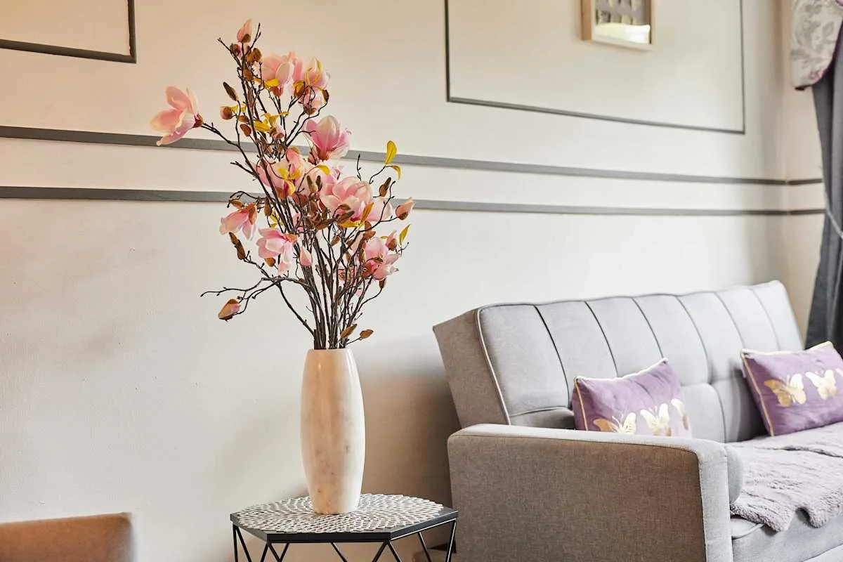 Una sala de estar con asientos y un jarrón con flores rosas.