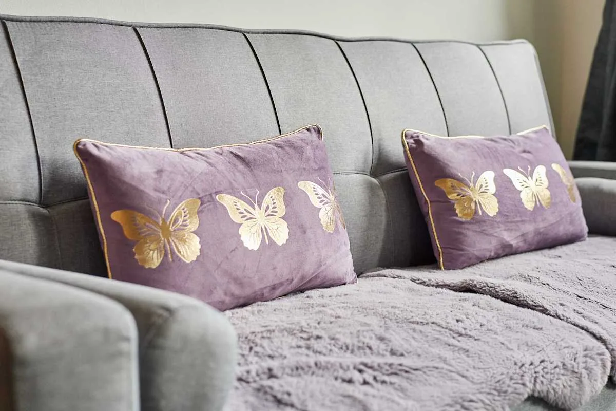 Un sofá tapizado gris con cojines morados estampados con mariposas.