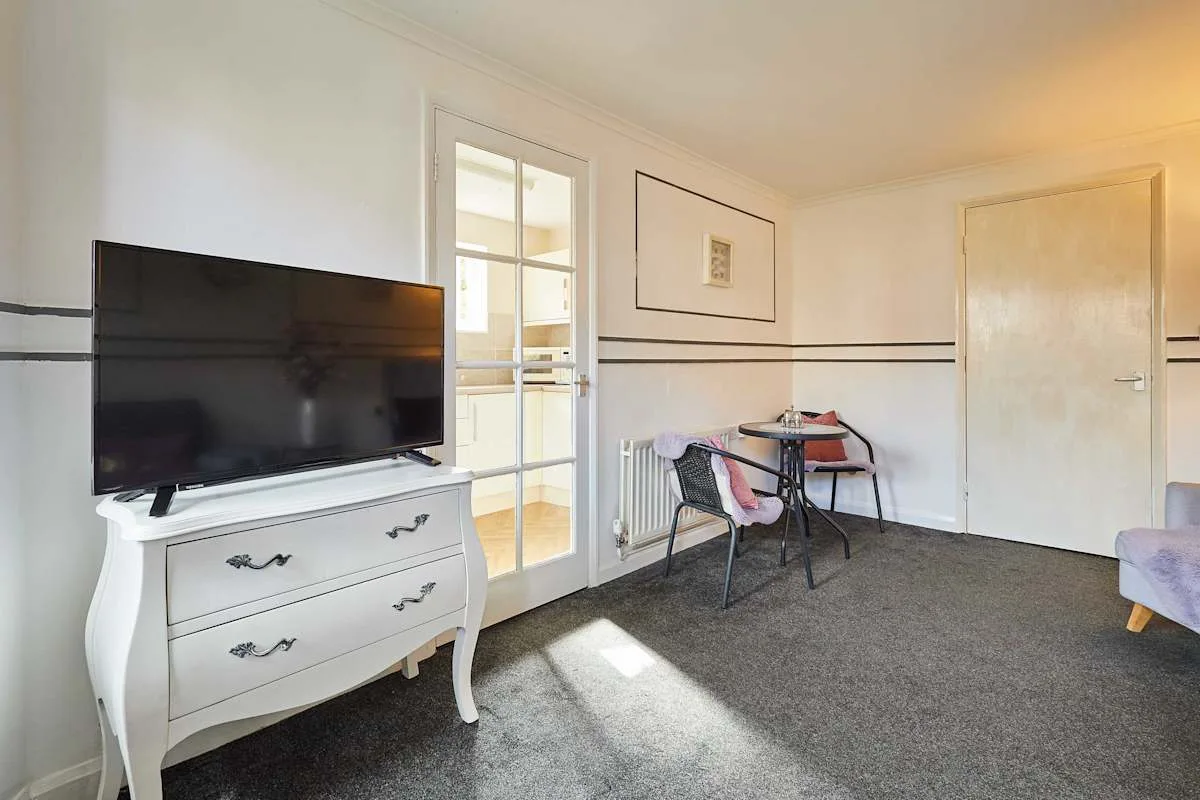 Una sala de estar con un televisor sobre una cómoda blanca y una mesa pequeña.