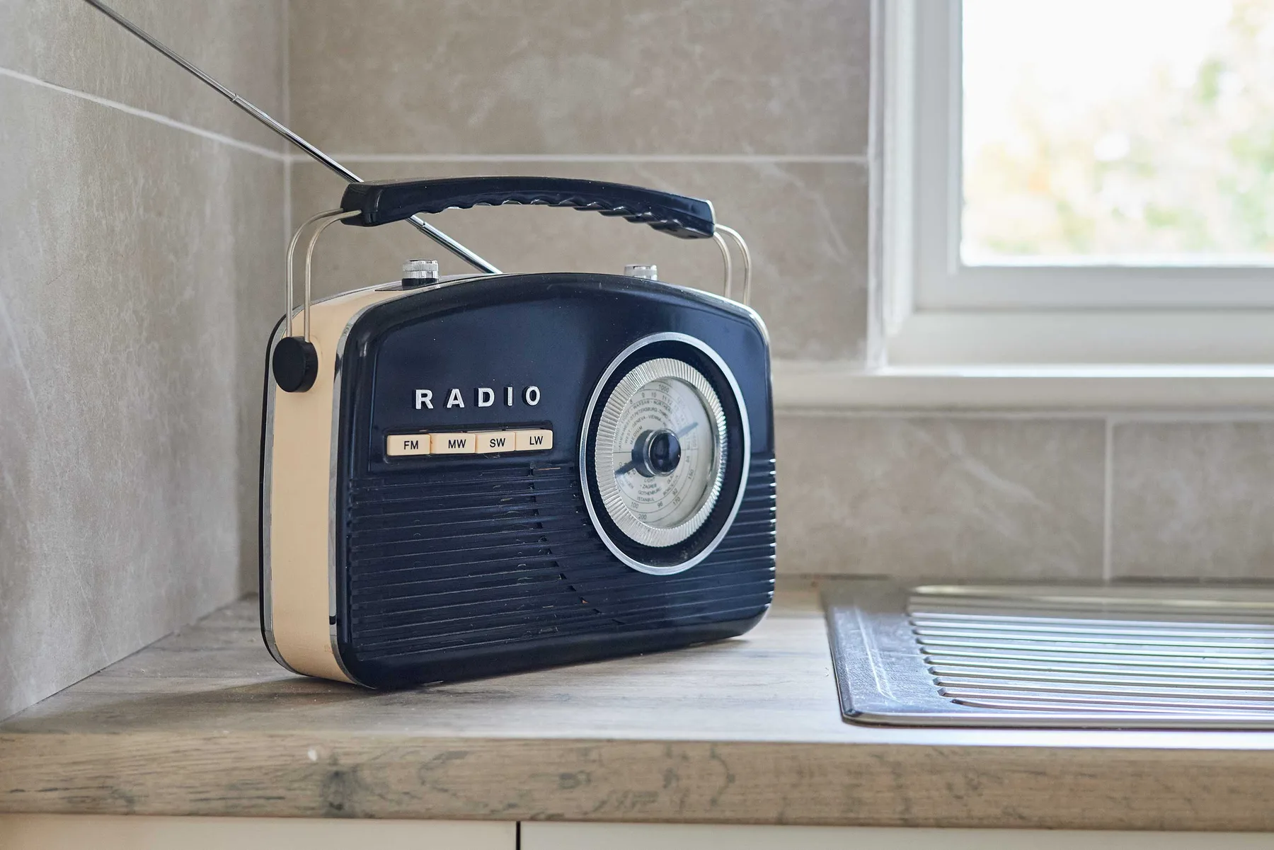 Una radio de estilo vintage está sobre una encimera junto a un fregadero metálico.