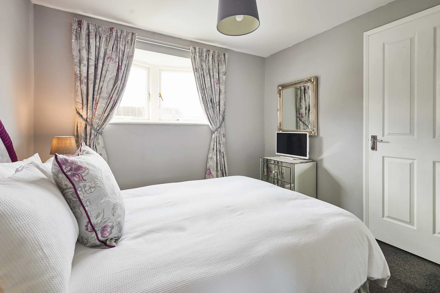 Un dormitorio con una cama bien tendida, una ventana y cortinas estampadas.