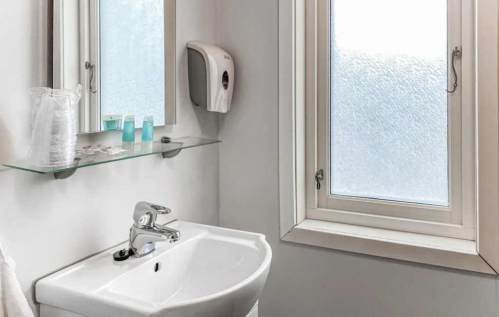 Un lavabo de baño está debajo de un espejo, junto a una ventana esmerilada.