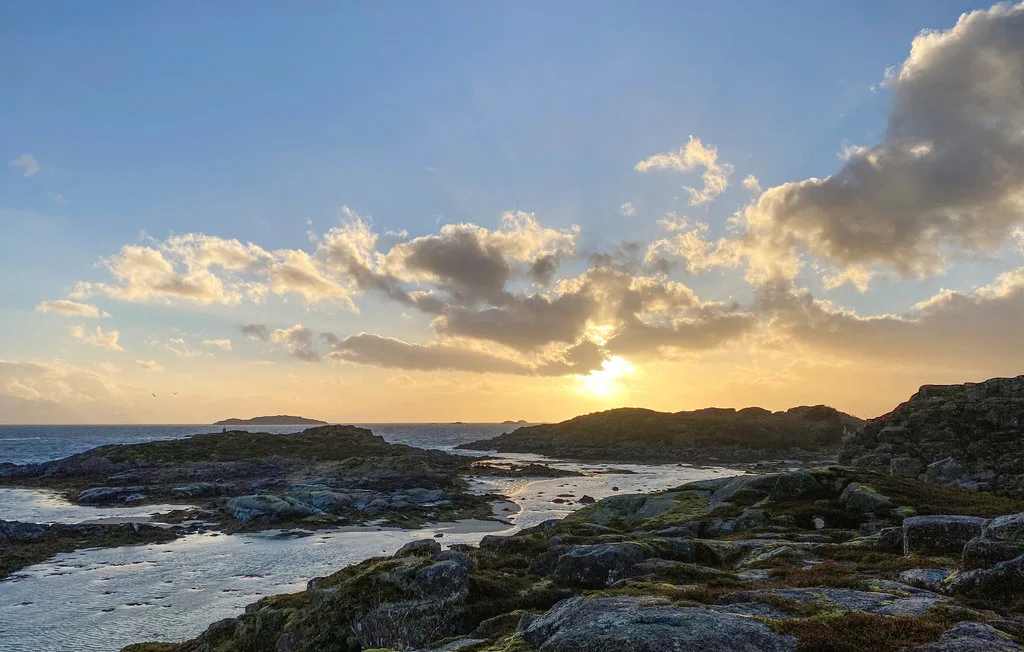 El atardecer ilumina una costa rocosa con charcos de agua poco profundos.