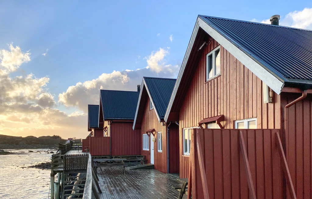 Red wooden cabins line a waterside deck beneath a bright evening sky.