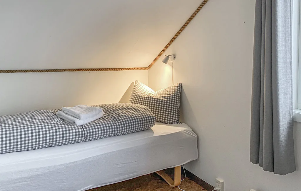 Una cama individual con ropa de cuadros y almohadas está bajo un techo inclinado.