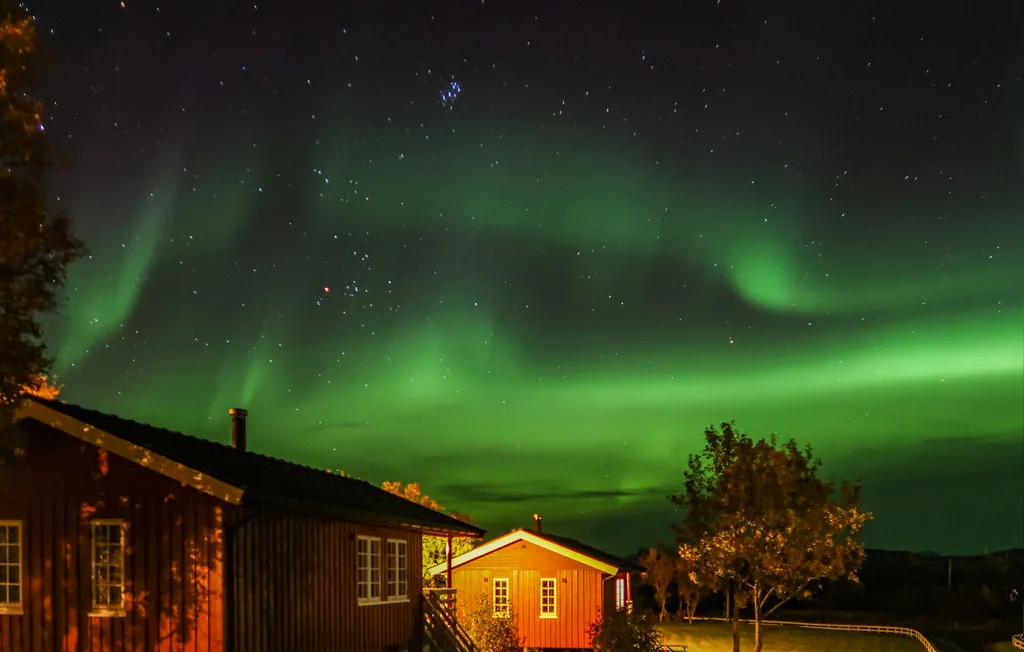 Una pequeña cabaña se encuentra bajo el resplandor verde de la aurora boreal.
