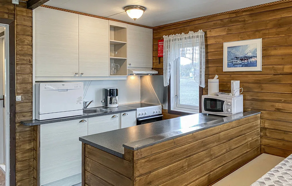 A compact kitchen with white cabinets, appliances, and a wood-paneled counter.