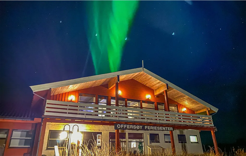 Un edificio de madera iluminado por la noche bajo auroras boreales verdes.