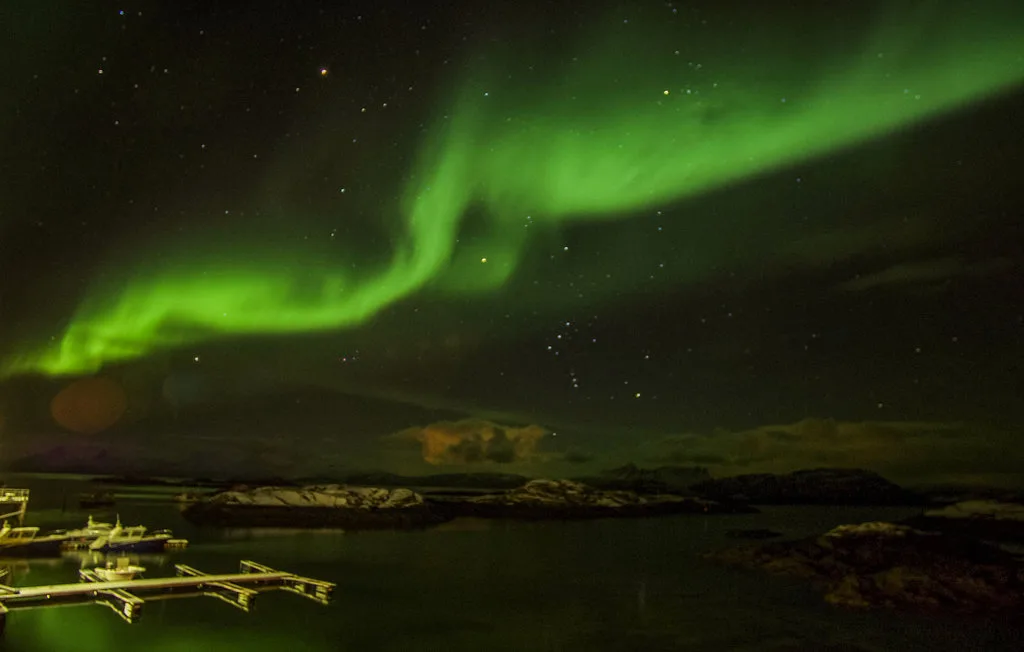 Paisaje nocturno con una aurora verde sobre una extensión de agua oscura.