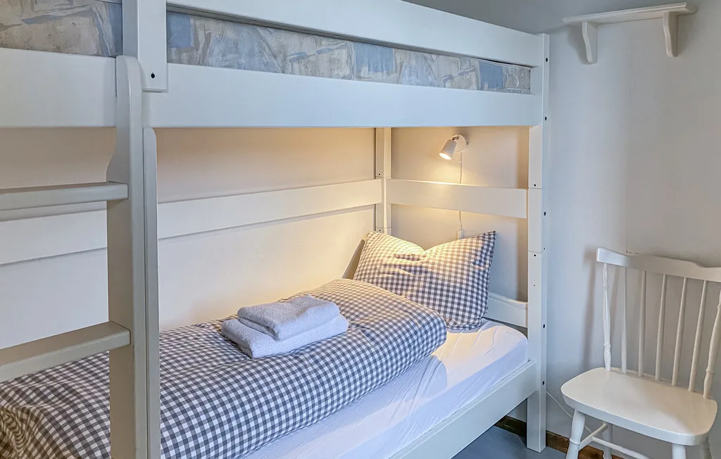Una litera con ropa de cama a cuadros y una silla blanca en un dormitorio.