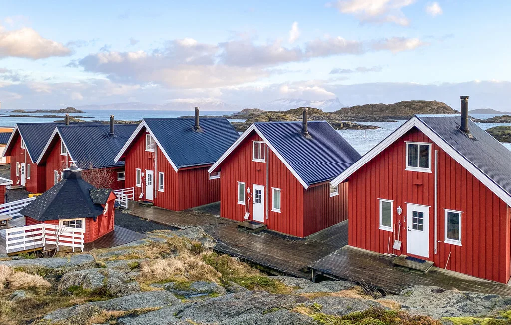 Red waterfront cabins with dark roofs sit beside rocky shoreline.