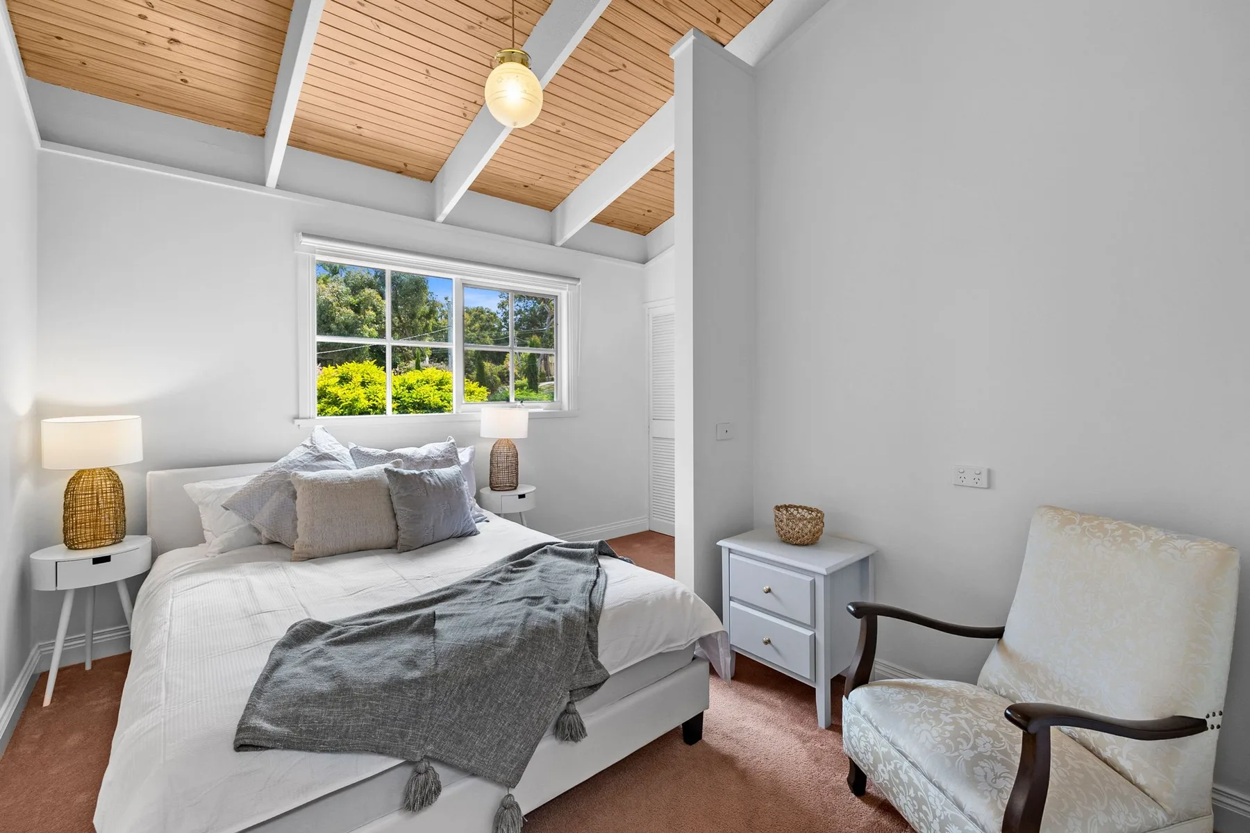 Un dormitorio luminoso con una cama, mesitas de noche y una ventana.