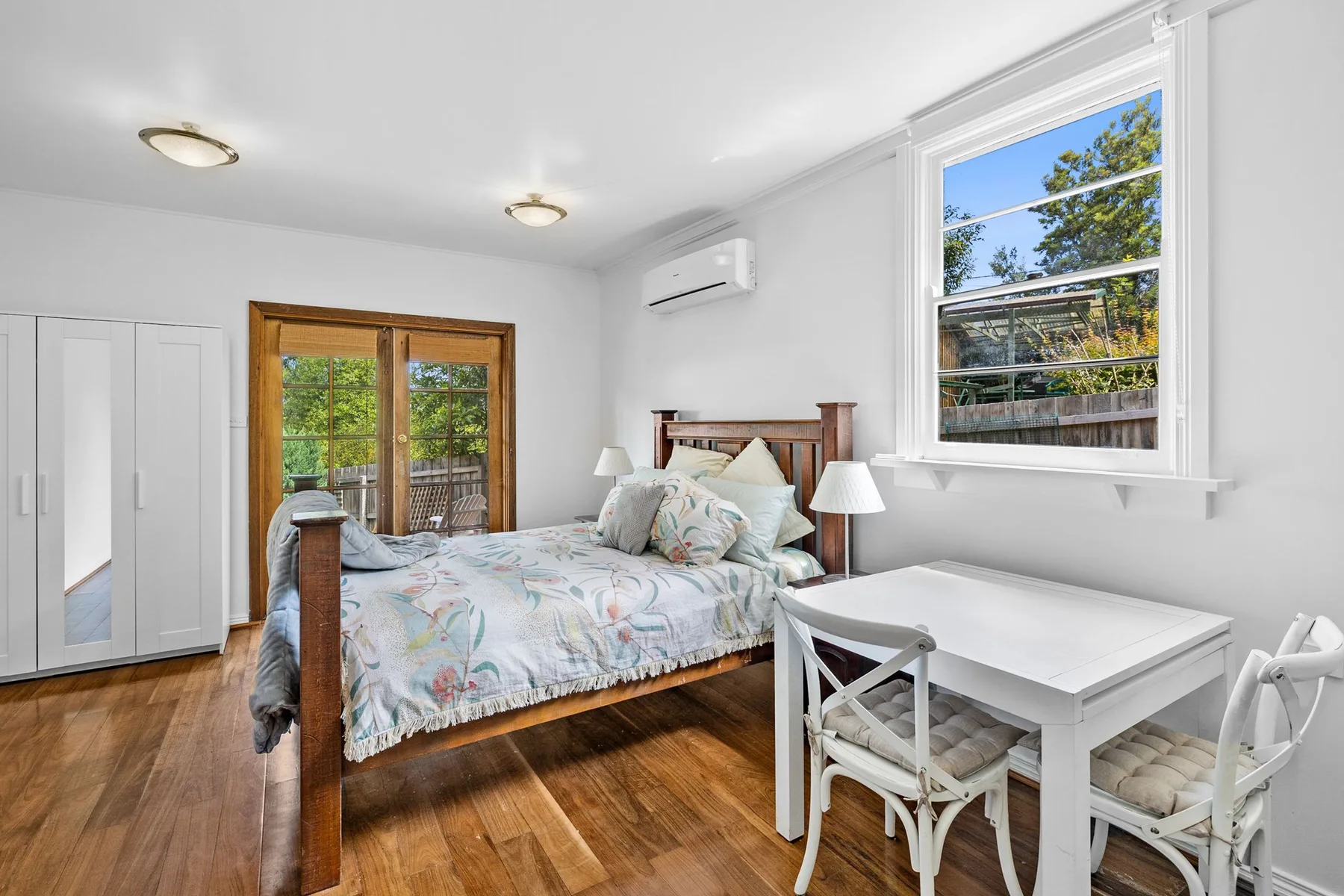 Dormitorio con una cama de madera y un escritorio blanco junto a la ventana.