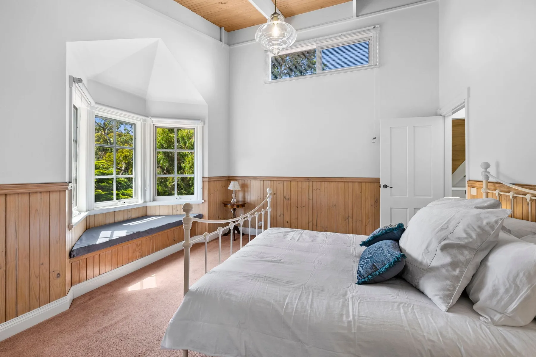 Un dormitorio luminoso con una cama blanca junto a un amplio ventanal.