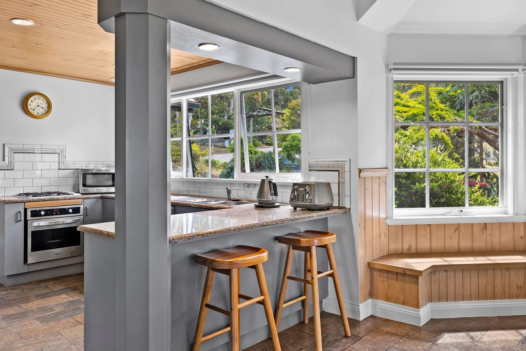 Una cocina luminosa con barra para desayunar y grandes ventanas con vistas a la vegetación.