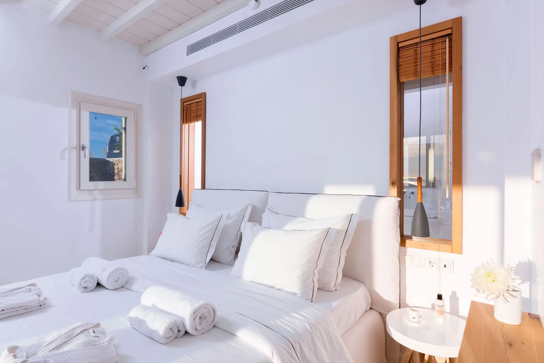Un dormitorio luminoso con ropa de cama blanca y ventanas altas con persianas de madera.
