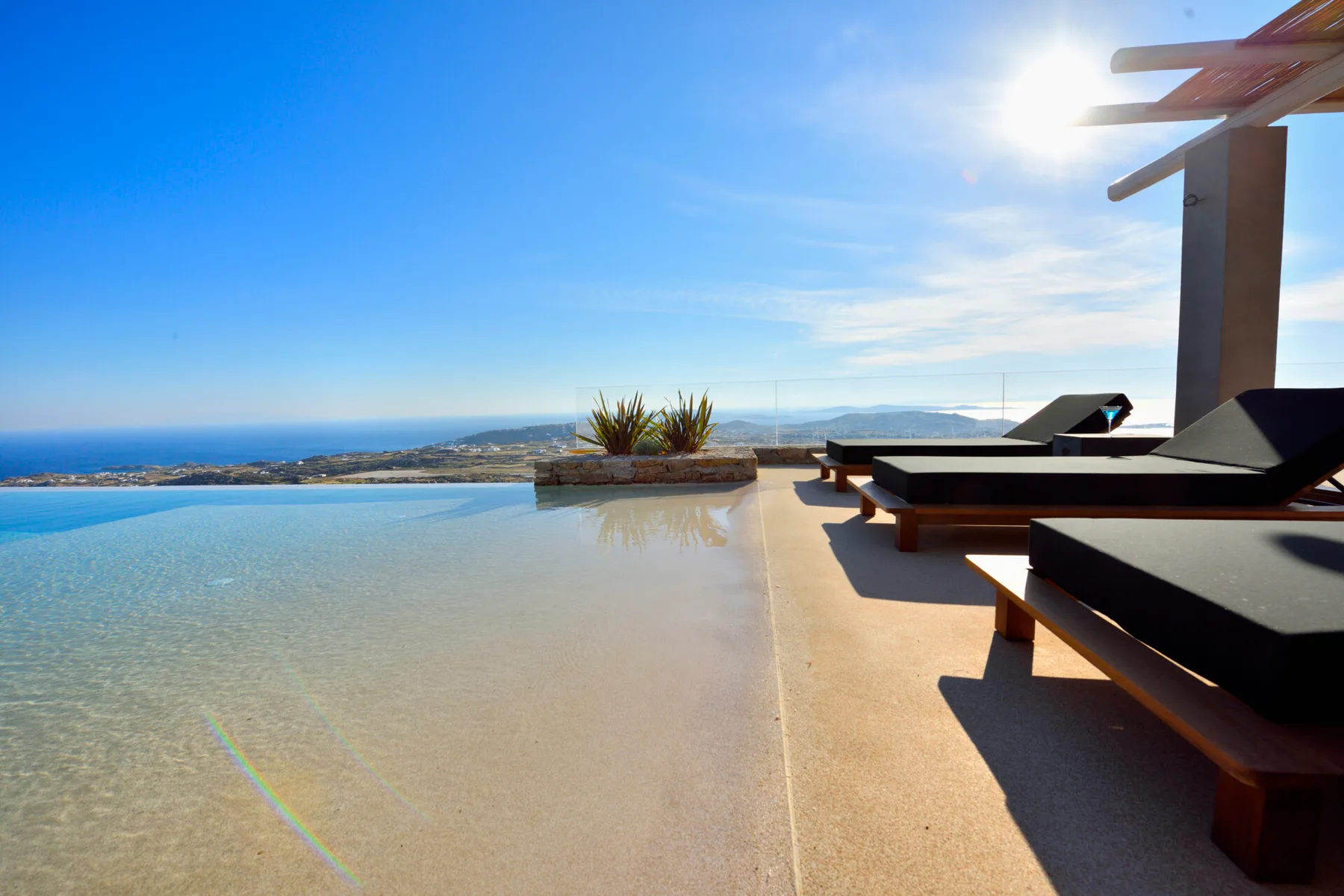 Una terraza soleada junto a la piscina tiene vistas al mar y asientos oscuros.
