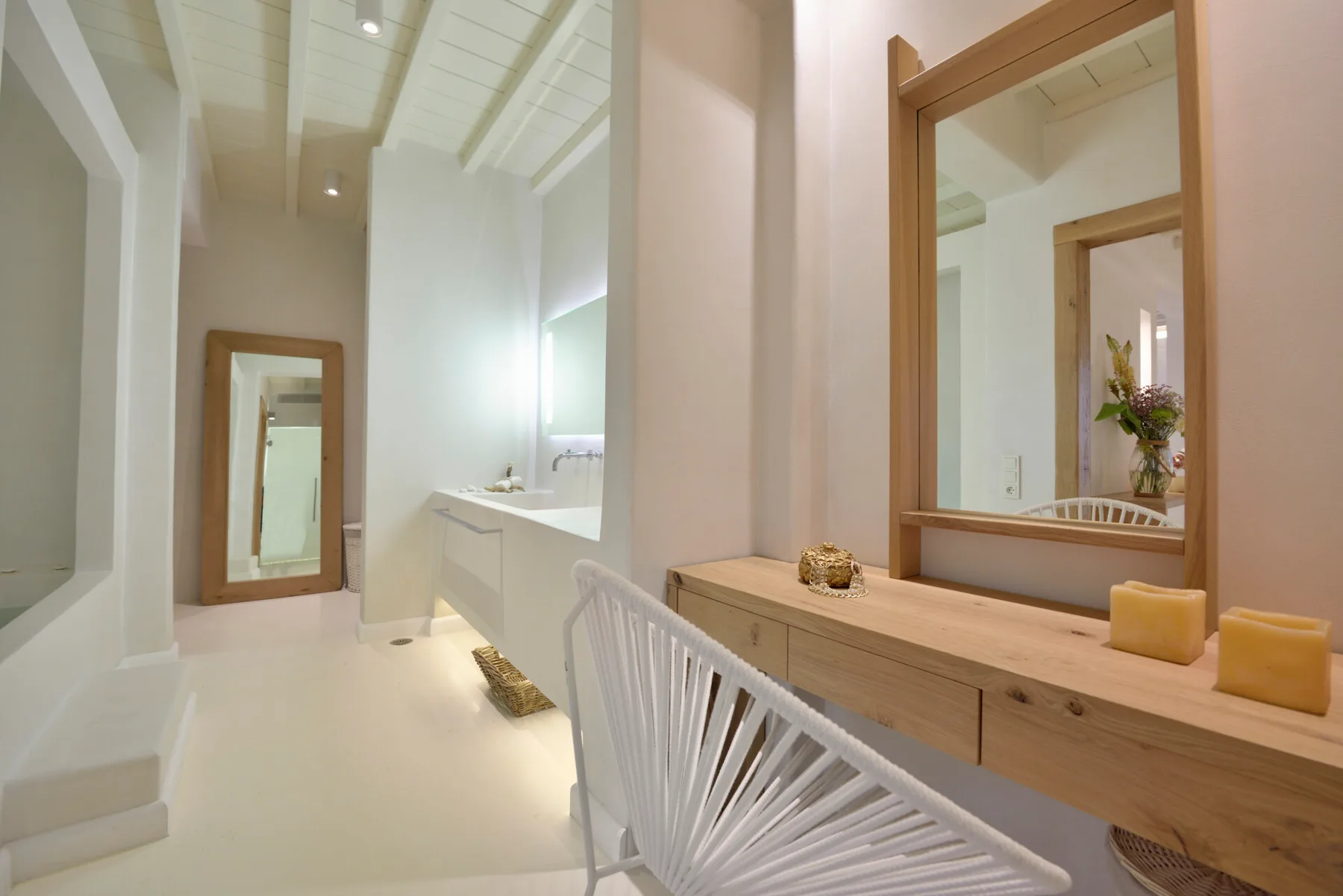 A bright bathroom with a long vanity, mirror, and white seating.