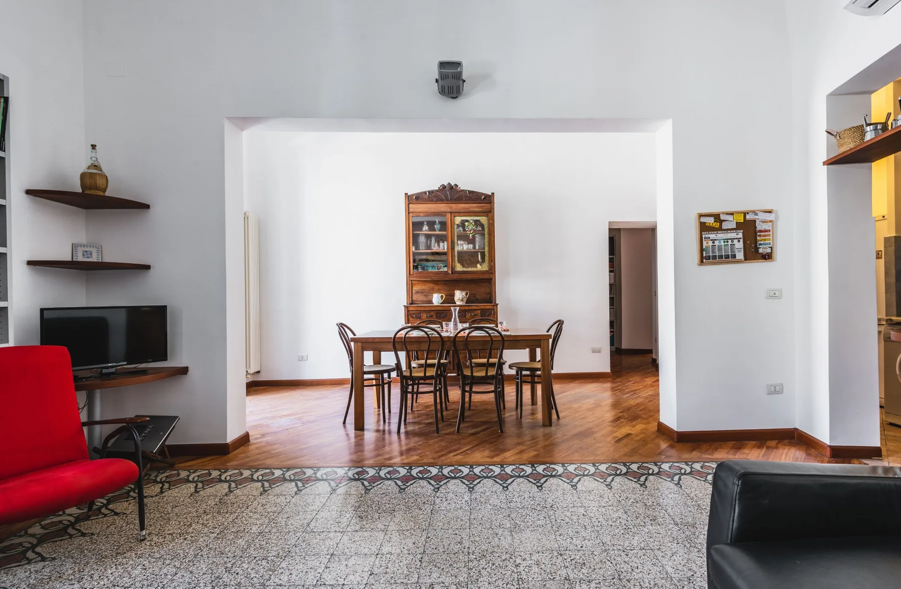 A living and dining area with a wooden table and chairs, a television, and a patterned rug.